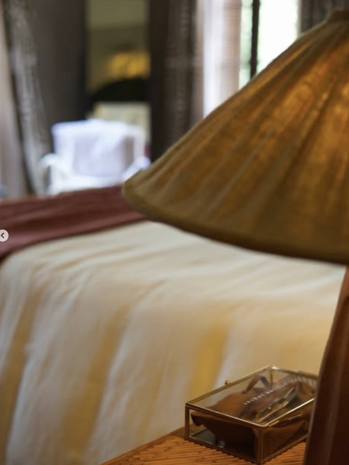 Canto de cama com manta em tom vinho iluminado por abajur de tecido