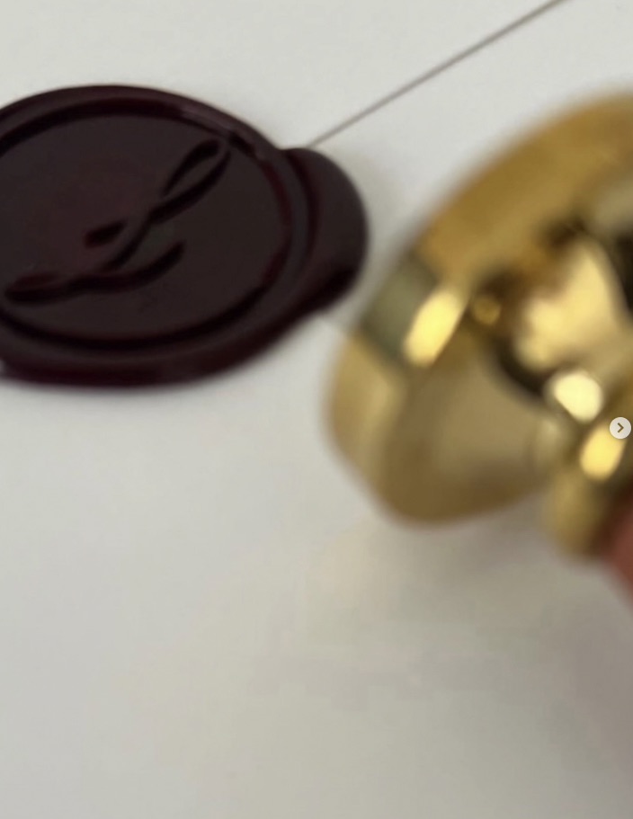 Lacre de cera oxblood com o monograma do atelier, ao lado do carimbo de latão